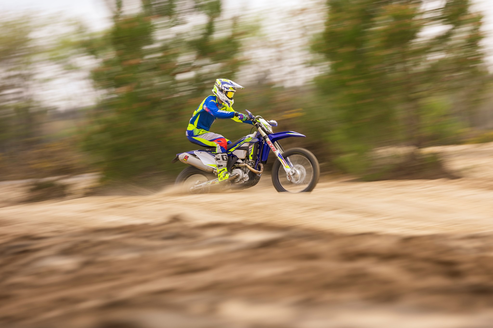 Piloto de enduro levantando tierra en un descenso, con el bosque desenfocado de fondo